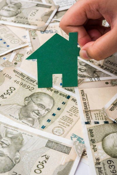 indian rupees and house model   in male hand isolated on  background