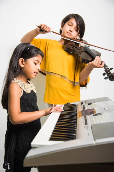 kids and music concept - indian little girls playing musical instruments like piano or keyboard or violin