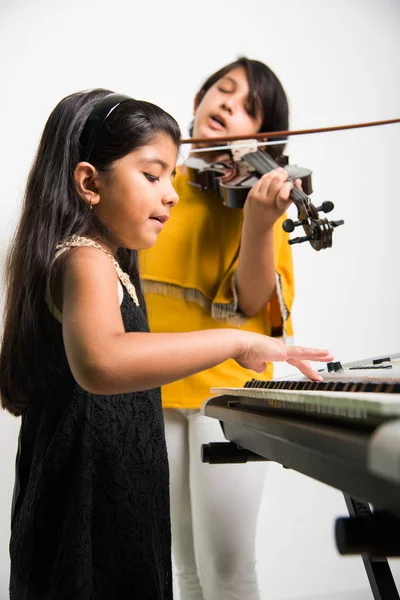 Kinder und Musikkonzept - kleine indische Mädchen spielen Musikinstrumente wie Klavier oder Keyboard oder Geige — Stockfoto