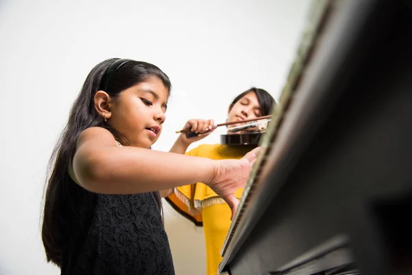 kids and music concept - indian little girls playing musical instruments like piano or keyboard or violin