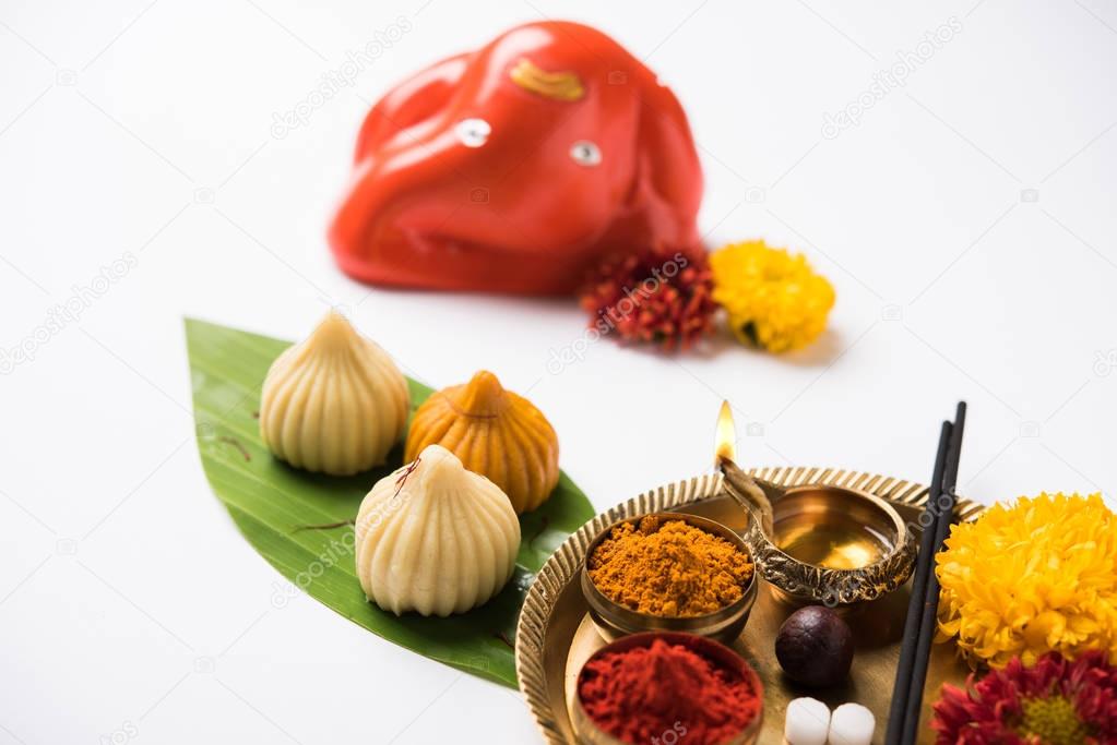 Indian Festival - Indian sweet food called Modak offered as prasad or prashad or chadhava  over green leaf to Lord Ganesha on Ganesh Chaturthi with puja or pooja thali and decorated with flowers