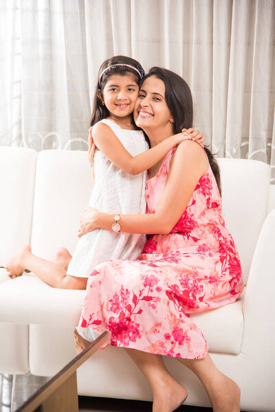 indian smart mother hugging her cute daughter, Portrait of happy Indian mother and daughter together while sitting on sofa