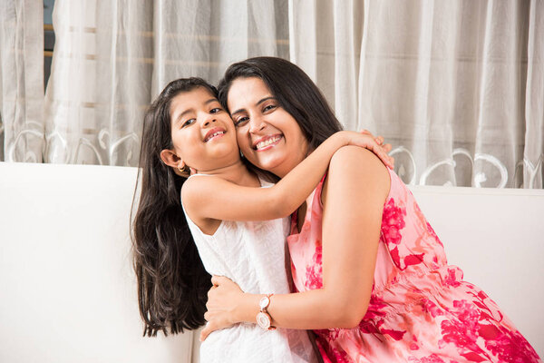indian smart mother hugging her cute daughter, Portrait of happy Indian mother and daughter together while sitting on sofa