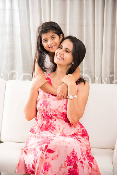 indian smart mother hugging her cute daughter, Portrait of happy Indian mother and daughter together while sitting on sofa