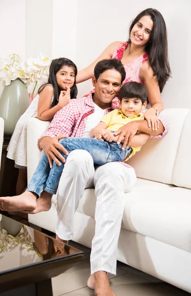 Candid Portrait of smart indian family of four while sitting on sofa. Indian or asian family group photo. Selective focus