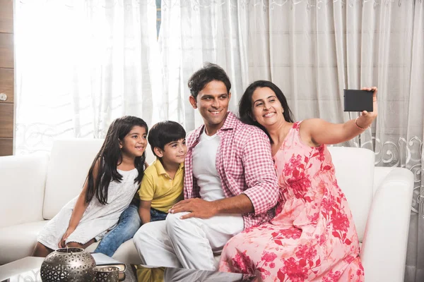 Családi idő - indiai család figyelembe selfie kép, csattanó-selfie smartphone, a boldog fiatal család négy, férj feleség, felesége és két gyerek, fedett, a kanapén ülve — Stock Fotó