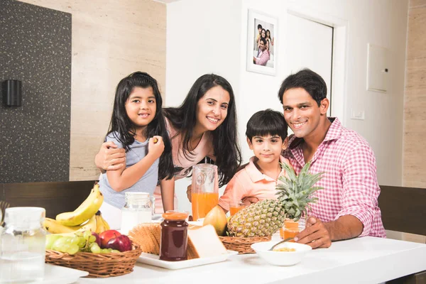 Uma atraente família indiana asiática feliz e sorridente de mãe, pai, filho e filha comendo comida saudável e salada em uma mesa de jantar. Índios tomando café da manhã, almoço ou jantar. Foco seletivo — Fotografia de Stock