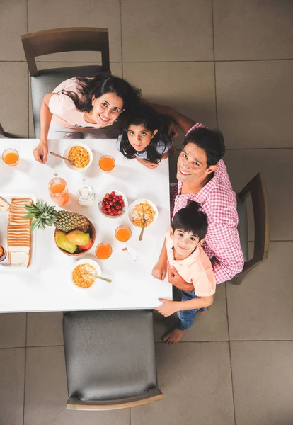 Top view of happy, smiling Asian Indian family of mother, father, son and daughter eating healthy food & salad at a dining table. Indians eating breakfast, lunch or dinner. Top view, Selective focus