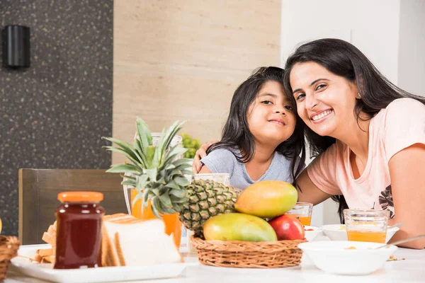 An attractive happy, smiling Asian Indian family of mother and daughter eating healthy food & salad at a dining table. Indians eating breakfast, lunch or dinner. Selective focus