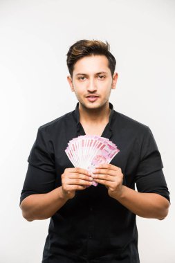 Beyaz arka planda tek başına dururken elinde banknot tutan yakışıklı Hintli adam.