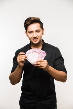 Beyaz arka planda tek başına dururken elinde banknot tutan yakışıklı Hintli adam.