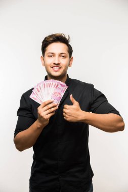 Beyaz arka planda tek başına dururken elinde banknot tutan yakışıklı Hintli adam.