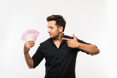 Beyaz arka planda tek başına dururken elinde banknot tutan yakışıklı Hintli adam.