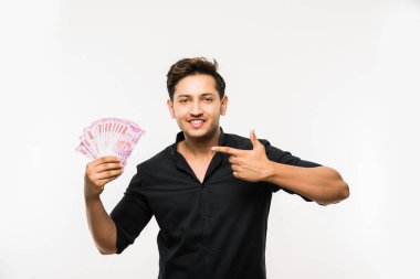 Beyaz arka planda tek başına dururken elinde banknot tutan yakışıklı Hintli adam.