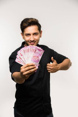 Beyaz arka planda tek başına dururken elinde banknot tutan yakışıklı Hintli adam.