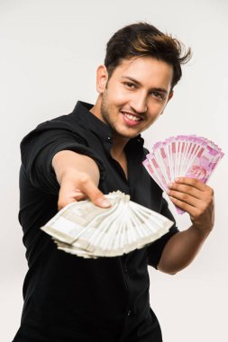 Beyaz arka planda tek başına dururken elinde banknot tutan yakışıklı Hintli adam.