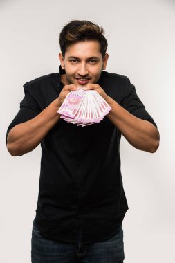 Beyaz arka planda tek başına dururken elinde banknot tutan yakışıklı Hintli adam.