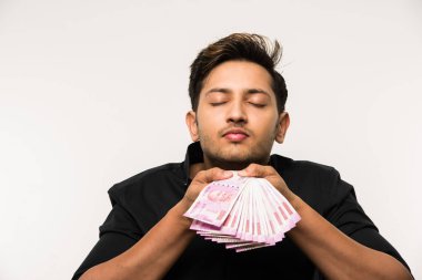 Beyaz arka planda tek başına dururken elinde banknot tutan yakışıklı Hintli adam.