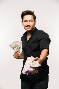 Beyaz arka planda tek başına dururken elinde banknot tutan yakışıklı Hintli adam.
