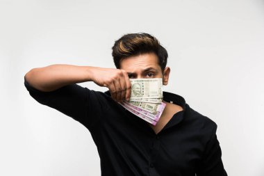 Beyaz arka planda tek başına dururken elinde banknot tutan yakışıklı Hintli adam.