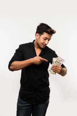 Beyaz arka planda tek başına dururken elinde banknot tutan yakışıklı Hintli adam.