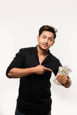 Beyaz arka planda tek başına dururken elinde banknot tutan yakışıklı Hintli adam.