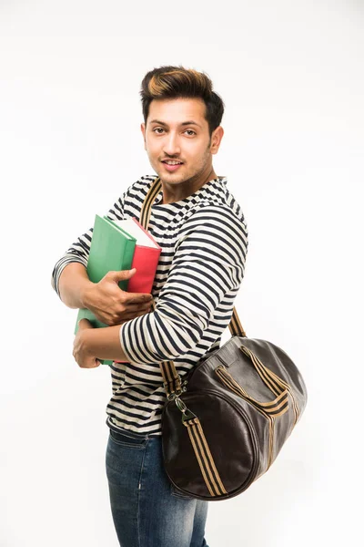 Красавчик и молодой индиец студент колледжа несет сумку на белом фоне, держа книги колледжа, ноутбук или смартфон — стоковое фото