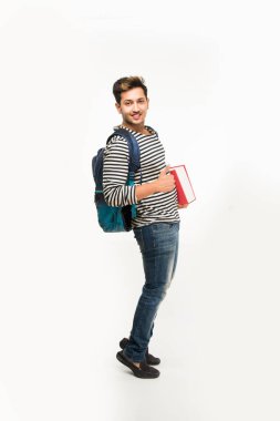 Yakışıklı ve genç Hintli erkek üniversite öğrencisi kolej kitaplar, dizüstü bilgisayar ya da akıllı telefon tutarak beyaz arka plan üzerinde çanta