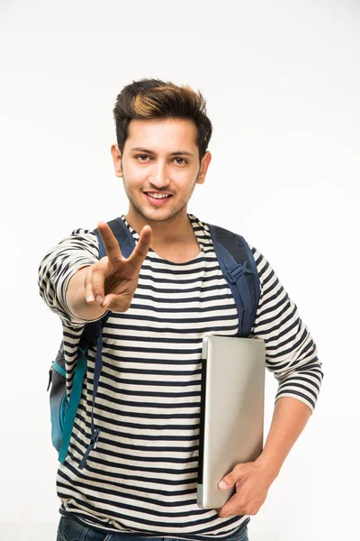 Handsome and young indian Male college student carrying bag on white background while holding college books, laptop or smart phone — Φωτογραφία Αρχείου