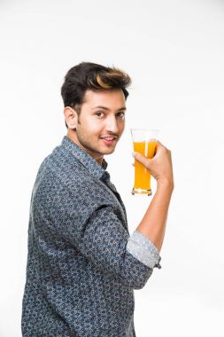 Genç yakışıklı Hintli adam rahat gömlek içme veya bir bardak taze portakal suyu veya kahvaltı için gazlı içecek dolu. 