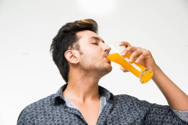 Genç yakışıklı Hintli adam rahat gömlek içme veya bir bardak taze portakal suyu veya kahvaltı için gazlı içecek dolu. 