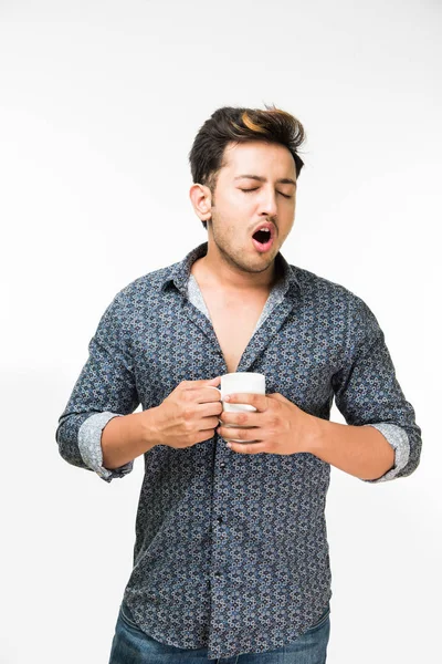 Esneme - esneme veya aynı anda beyaz arka plan üzerinde izole ayakta uykulu hissediyorum bir fincan kahve sahip genç yakışıklı bir Hintli adam portresi