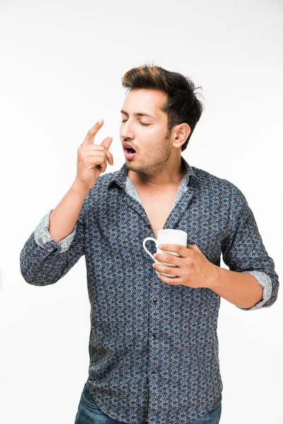 Gäspningar - porträtt av en ung stilig indiska man ha en kopp kaffe medan gäspningar eller sömnighet på samma gång, står isolerade över vit bakgrund — Stockfoto