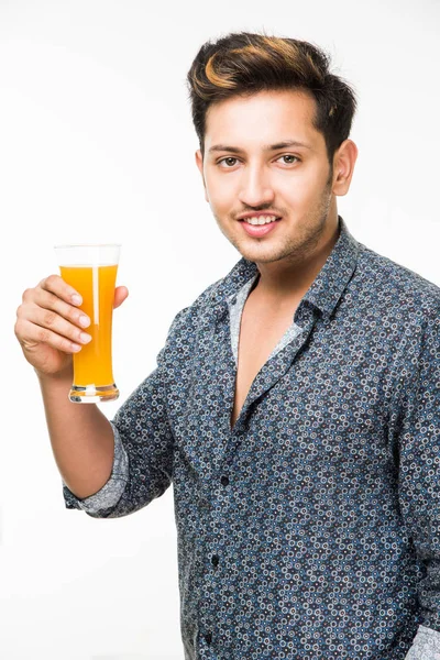 Genç yakışıklı Hintli adam rahat gömlek içme veya bir bardak taze portakal suyu veya kahvaltı için gazlı içecek dolu. 