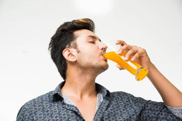 Genç yakışıklı Hintli adam rahat gömlek içme veya bir bardak taze portakal suyu veya kahvaltı için gazlı içecek dolu. 