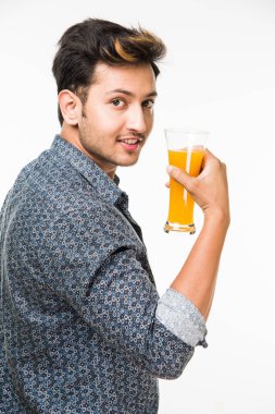 Genç yakışıklı Hintli adam rahat gömlek içme veya bir bardak taze portakal suyu veya kahvaltı için gazlı içecek dolu. 