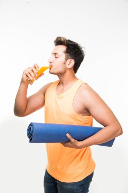 Hintli genç yakışıklı adam holding yoga ya da egzersiz minderi ve cam sonrası egzersiz veya yoga taze meyve suyu bir yudum sahip / asana, izole beyaz arka plan üzerinde