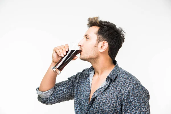 Genç yakışıklı Hintli adam rahat gömlek içme veya bir bardak taze portakal suyu veya kahvaltı için gazlı içecek dolu. 