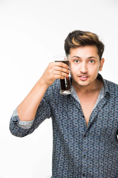 Genç yakışıklı Hintli adam rahat gömlek içme veya bir bardak taze portakal suyu veya kahvaltı için gazlı içecek dolu. 