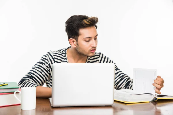 Przystojny chłopak Indian lub mężczyzna student studia studium tabela z stos książek, laptop komputer i kawa kubek. Uśmiechający się lub myślenia lub martwi się lub pokazuje kciuk w lub przy użyciu smartfona — Zdjęcie stockowe