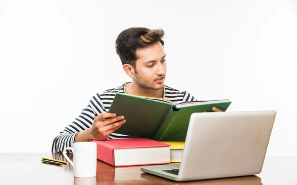 Beau garçon indien ou étudiant étudiant étudiant sur la table d'étude avec pile de livres, ordinateur portable et tasse à café. Sourire ou penser ou s'inquiéter ou montrer les pouces vers le haut ou en utilisant un smartphone — Photo