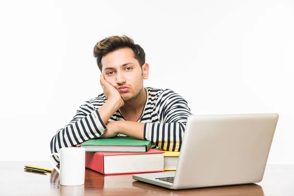 Beau garçon indien ou étudiant étudiant étudiant sur la table d'étude avec pile de livres, ordinateur portable et tasse à café. Sourire ou penser ou s'inquiéter ou montrer les pouces vers le haut ou en utilisant un smartphone — Photo