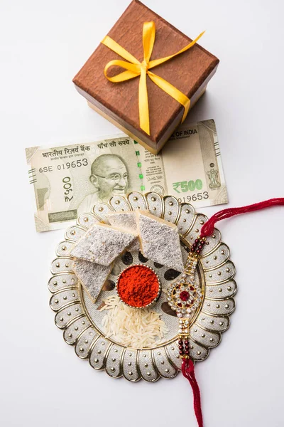 Salut Raksha Bandhan - Rakhi și cadou cu kaju katli dulce sau mithai și cereale de orez și kumkum într-o farfurie decorativă. Trupa tradițională indiană de încheietura mâinii este un simbol al iubirii dintre frați și surori. — Fotografie, imagine de stoc