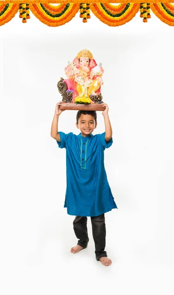 Porträtt av söt liten indisk pojke håller en Ganesh idol eller lord ganesha eller ganapati murti /statue över huvudet, tog hem på Ganesh Chaturthi, isolerade över vit bakgrund — Stockfoto