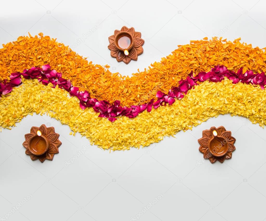 flower rangoli for Diwali or pongal made using marigold or zendu flowers and red rose petals over white background with diwali diya in the middle, selective focus