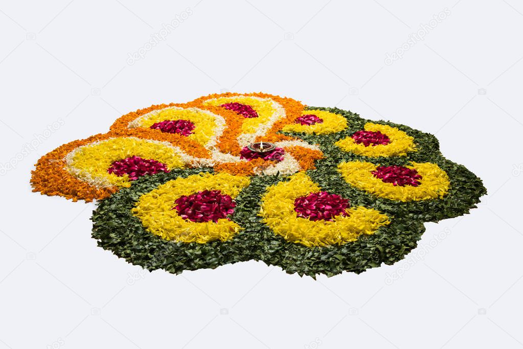 flower rangoli for Diwali or pongal or onam made using marigold or zendu flowers and red rose petals over white background with diwali diya in the middle, selective focus