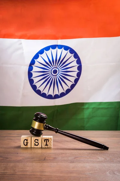 Foto de stock de GST baja en la India. GST texto escrito sobre bloques de madera con mazo de madera sobre ella y bandera nacional india o tricolor en el fondo, enfoque selectivo — Foto de Stock
