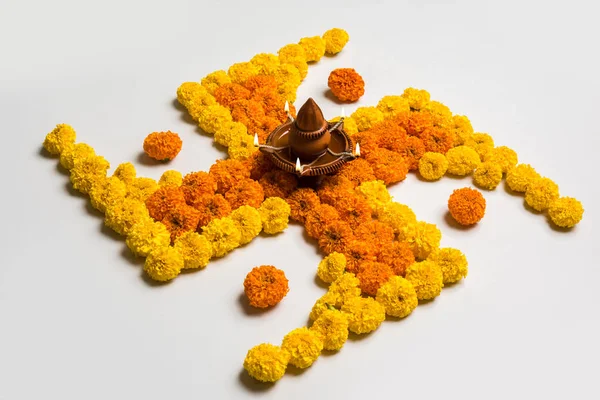 Φωτογραφία απόθεμα των Ινδουιστών ευοίωνο σύμβολο που ονομάζεται σβάστικα ή swastik που γίνονται χρησιμοποιώντας το marigold λουλούδι/zendu/ατζέντας ύμνος & diwali diya / φανός πηλό, rangoli λουλούδι σε σχήμα σβάστικα για diwali/pongal/onam — Φωτογραφία Αρχείου