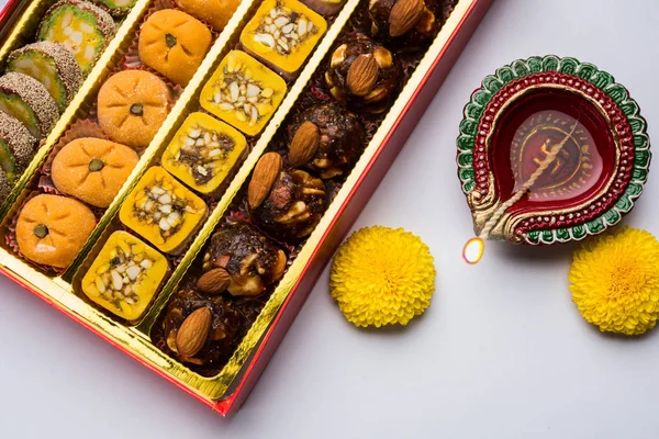 Stockfoto van Indiase zoete mithai en olie lamp of diya met luxe-geschenketui en bloemen op decoratieve of kleurrijke achtergrond, selectieve aandacht — Stockfoto
