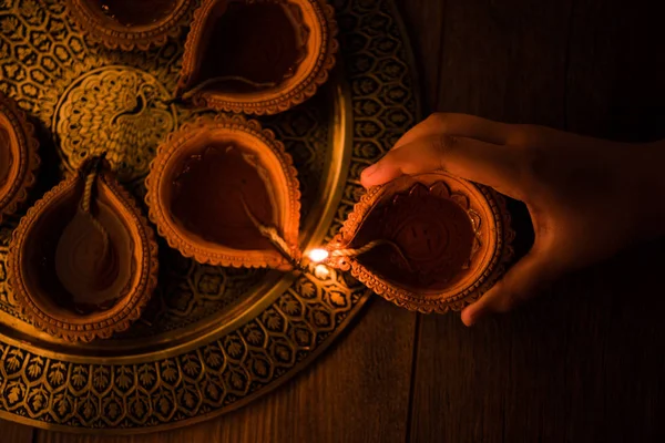 Ευτυχισμένο diwali - χέρι εκμετάλλευση ή φωτισμού Τακτοποιώντας diya ή πηλό λάμπα diwali στην πλάκα ορείχαλκου, επιλεκτική εστίαση — Φωτογραφία Αρχείου